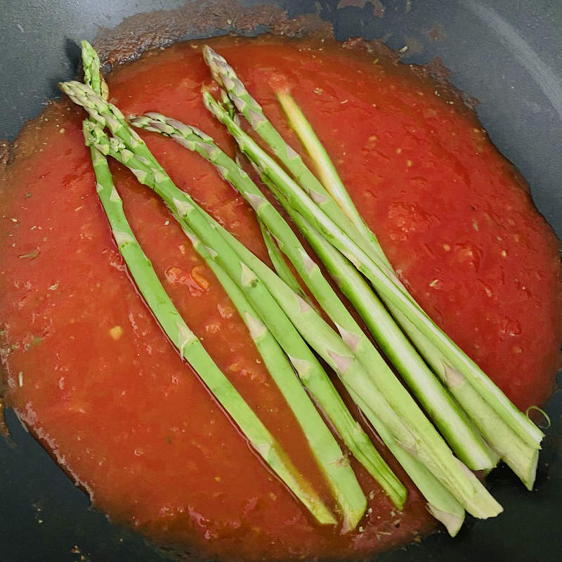 縦に切ったアスパラガスを、トマトピューレに加えて、アスパラガスがやわらかくなるまで煮る。