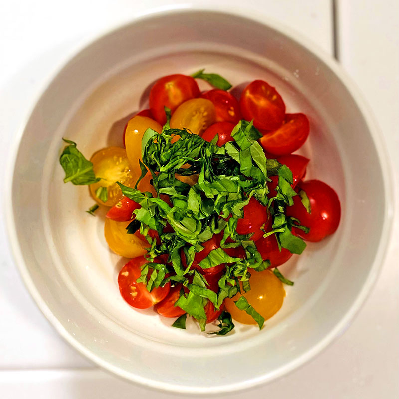 Put the halved tomatoes into the bowl, add chopped basil and mix them.