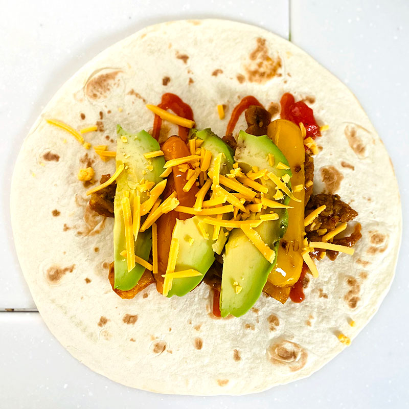 Warm up the tortillas and add the SoMeat with cherry tomatoes, sliced avocado and cheese on top, then, roll to make a SoMeat Tortilla Wrap.